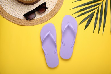 Stylish flip flops, sunglasses, hat and palm leaf on yellow background, flat lay