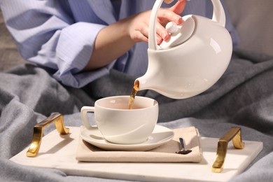 Photo of Woman pouring aromatic tea into cup at table, closeup