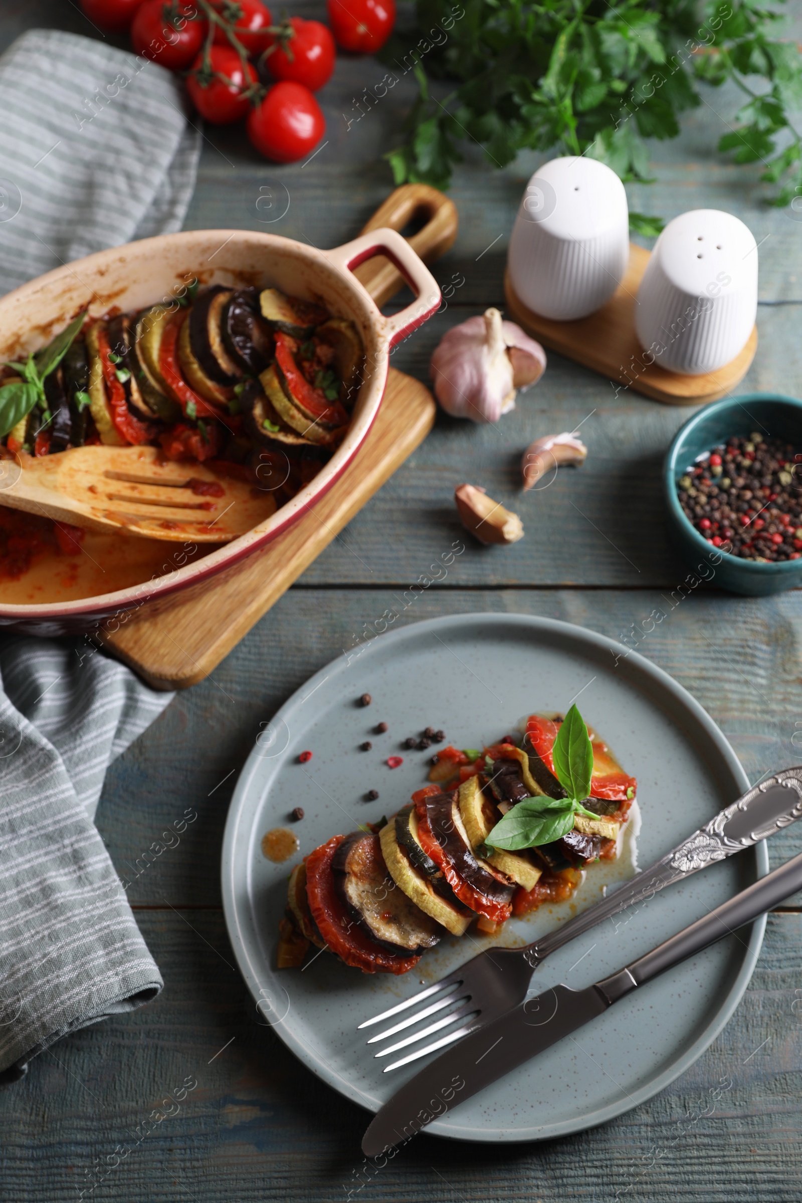 Photo of Delicious ratatouille served with basil on grey wooden table, above view