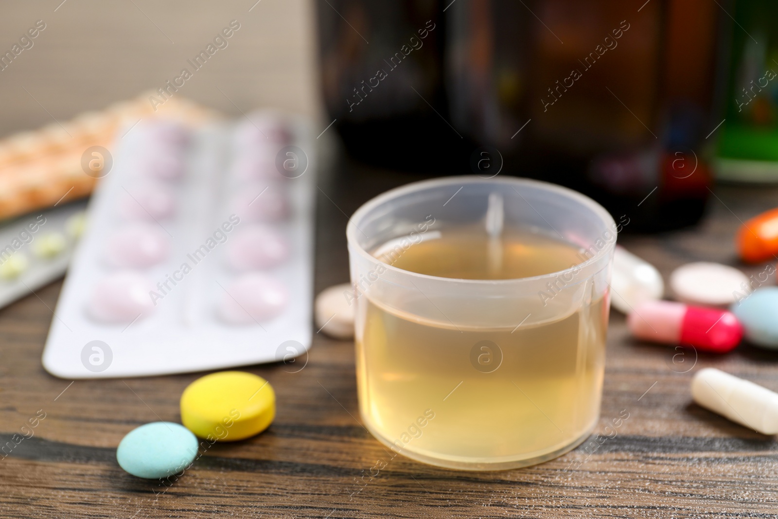 Photo of Measuring cup with syrup and pills on wooden table, closeup. Cold medicine