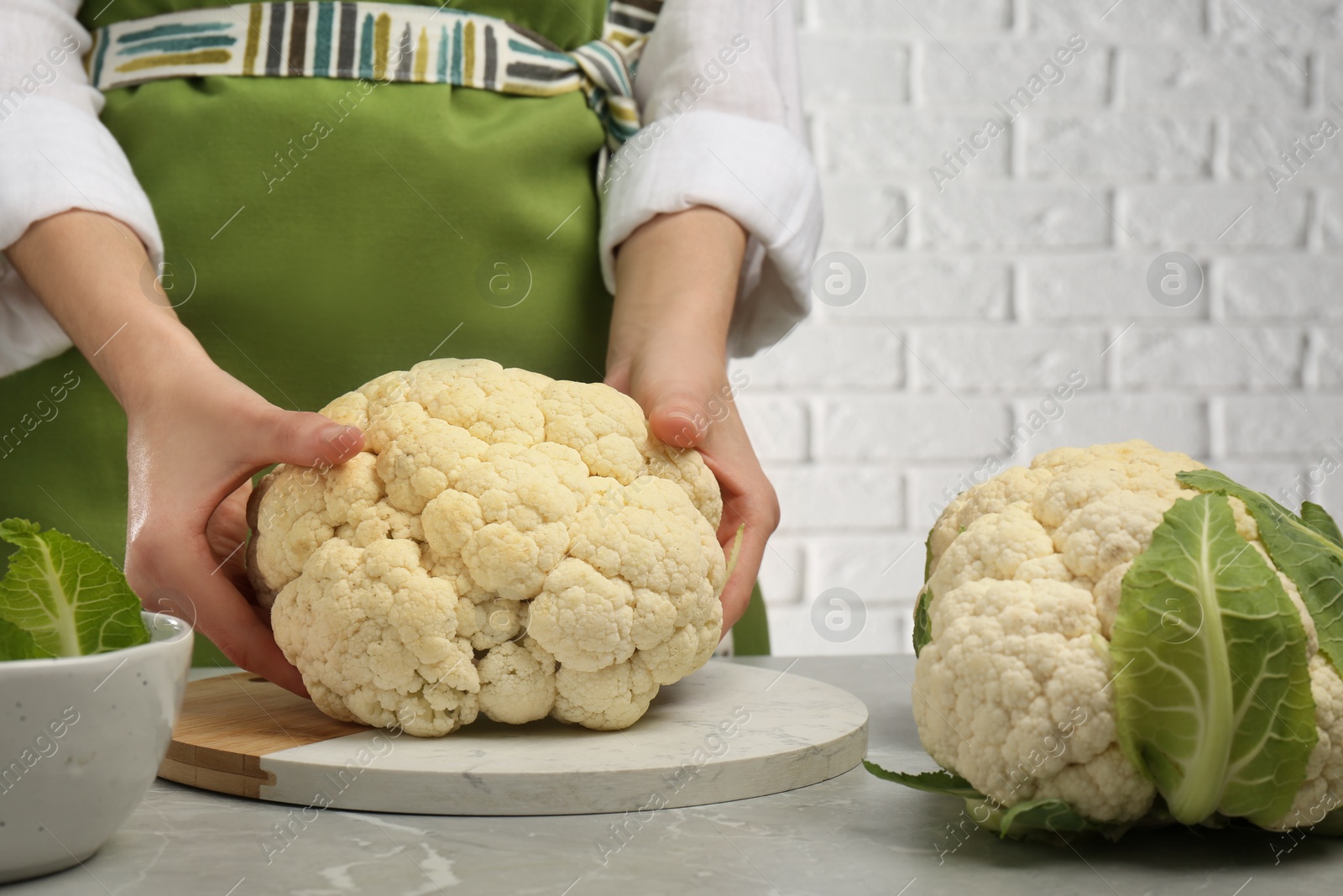 Photo of Woman with fresh cauliflower at light grey table, closeup