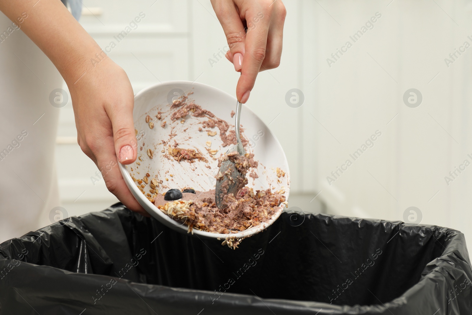 Photo of Woman throwing oatmeal with berries into bin indoors, closeup