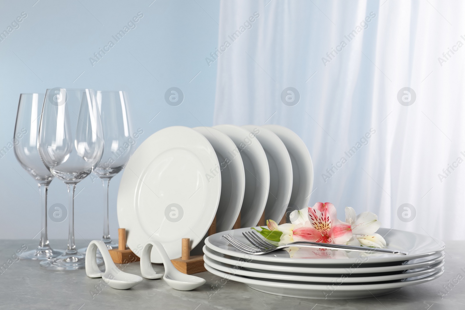 Photo of Glasses and clean dishware with flowers on grey marble table