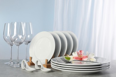 Glasses and clean dishware with flowers on grey marble table