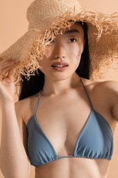 Photo of Beautiful young woman in straw hat with sun protection cream on her face against beige background