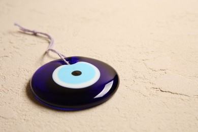 Photo of Evil eye amulet on beige textured table, closeup. Space for text