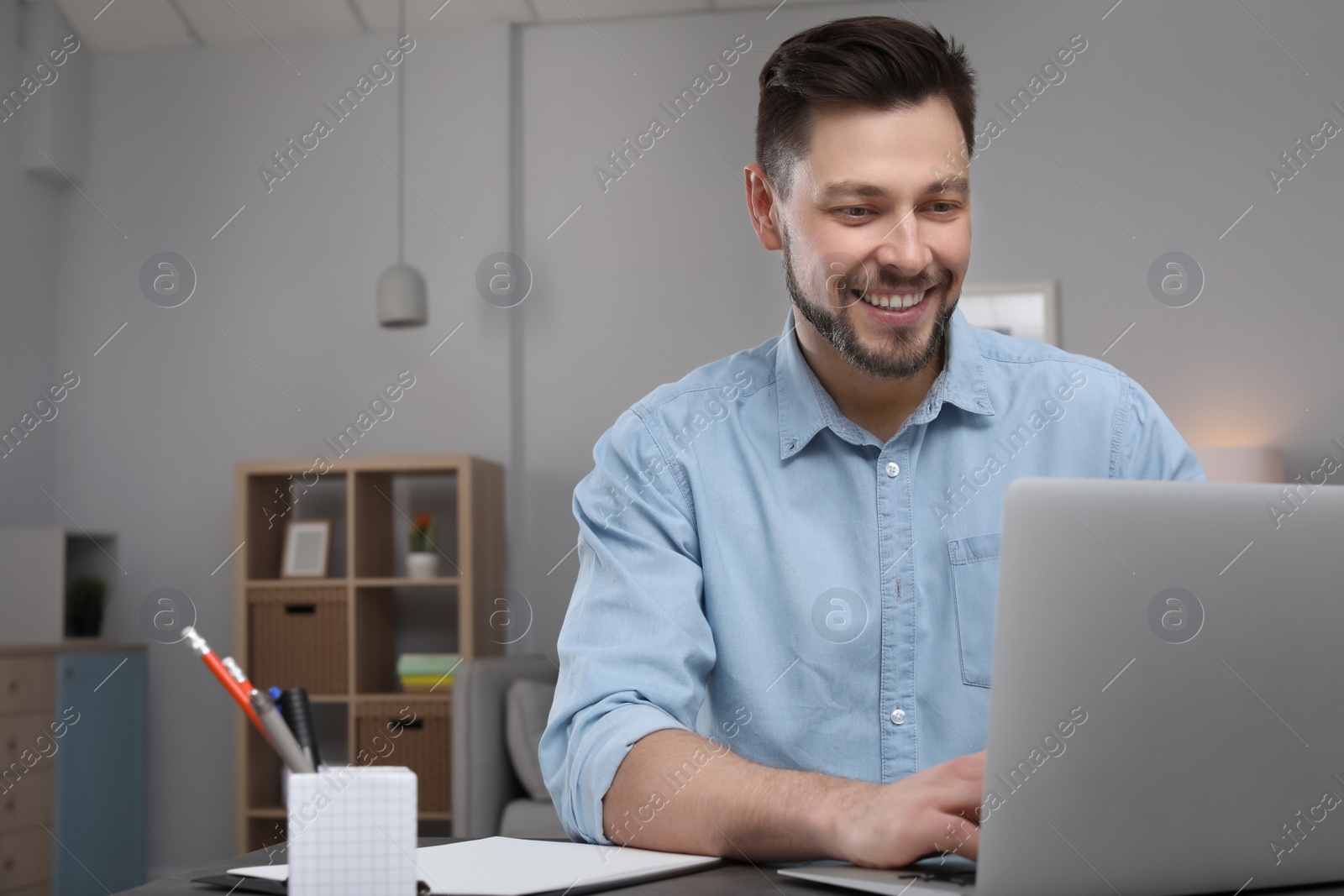 Photo of Young man working with laptop at desk in home office