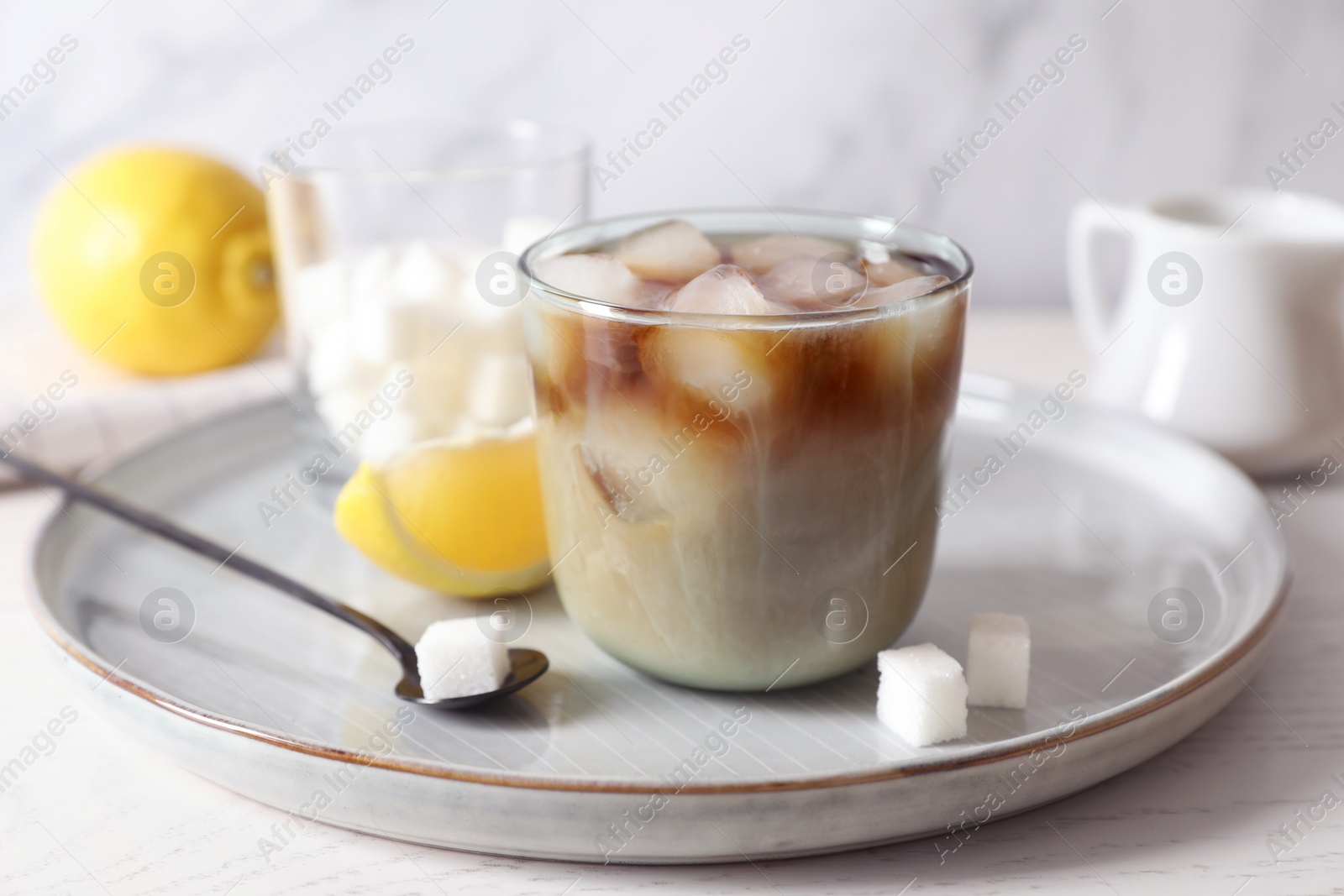 Photo of Refreshing iced coffee with milk in glass, sugar cubes and spoon on white wooden table, closeup