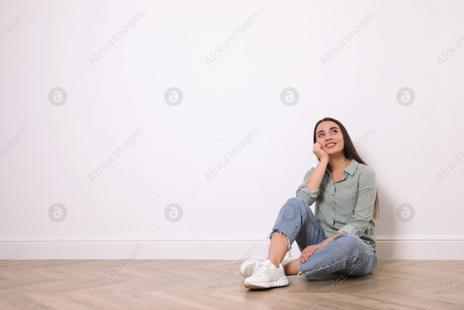 Photo of Young woman sitting on floor near white wall indoors. Space for text