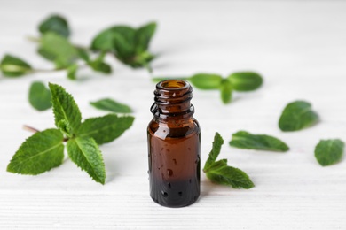 Bottle of mint essential oil on white wooden table