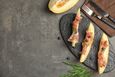 Photo of Flat lay composition of fresh melon with prosciutto on grey table. Space for text