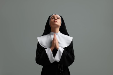 Photo of Nun with clasped hands praying to God on grey background