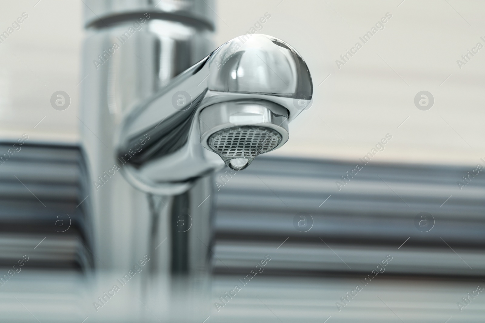 Photo of Water drop falling down from tap on blurred background, closeup. Space for text