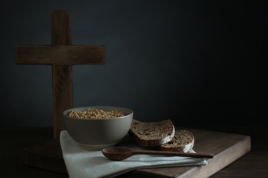 Photo of Oatmeal porridge, bread and cross on wooden table, space for text. Lent season