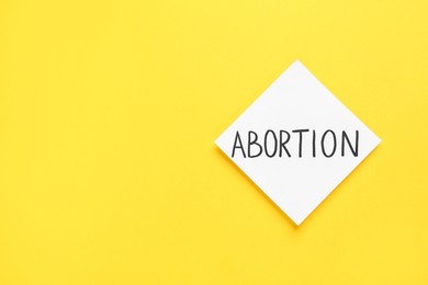 Photo of Paper note with word Abortion on yellow background, top view. Space for text