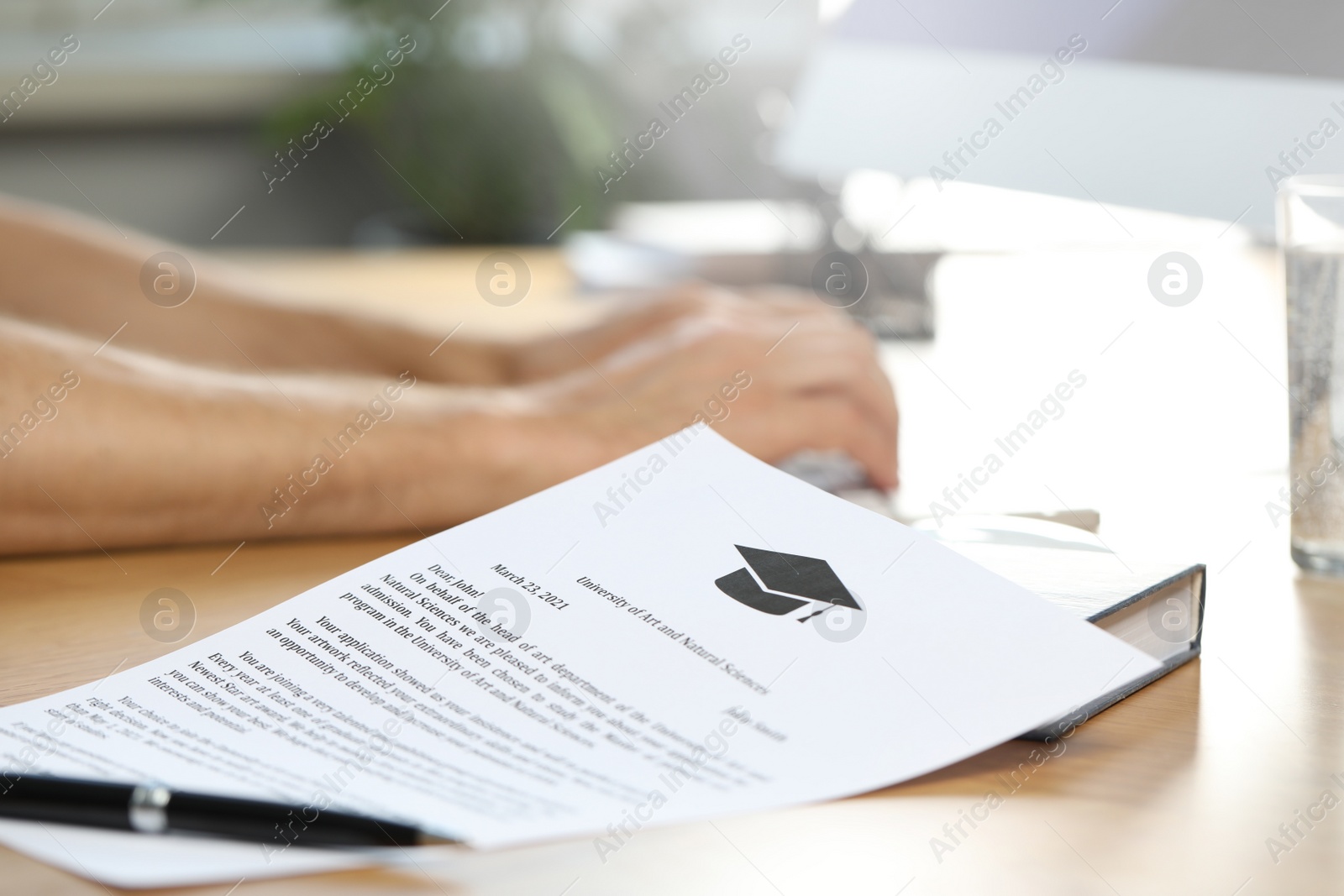 Photo of Student using computer at wooden table indoors, focus on acceptance letter from university