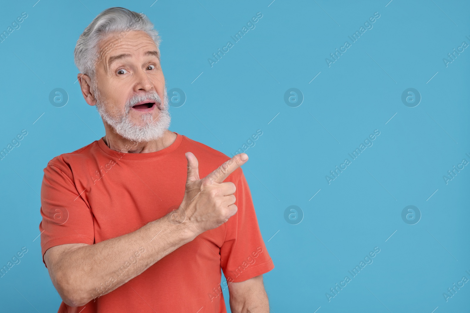 Photo of Surprised senior man pointing at something on light blue background, space for text