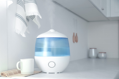 Photo of Modern air humidifier, cup and bamboo mat on counter in kitchen. Space for text