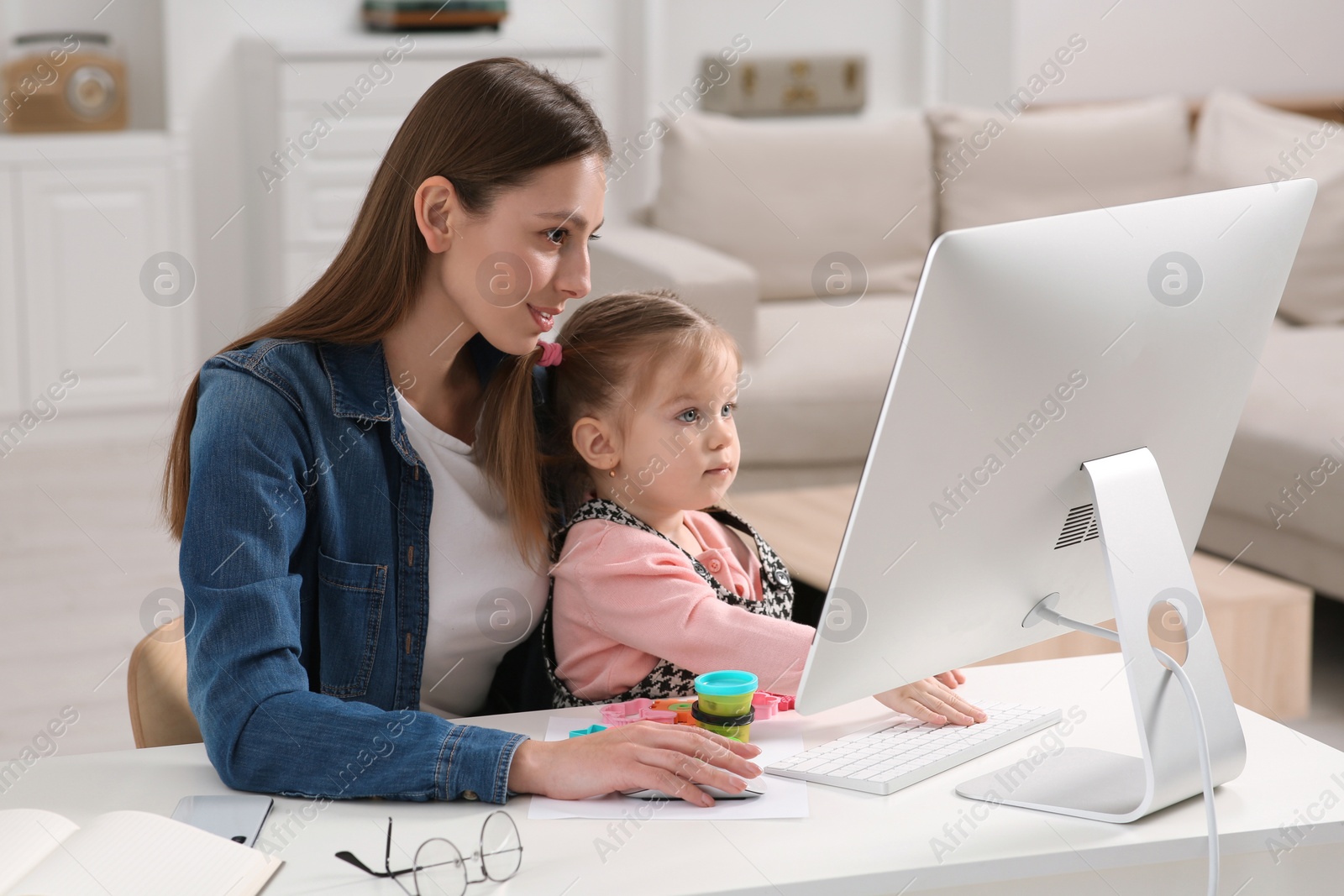 Photo of Woman working remotely at home. Mother and her daughter at desk with computer