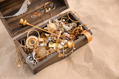 Photo of Open wooden chest with treasures on sand, above view