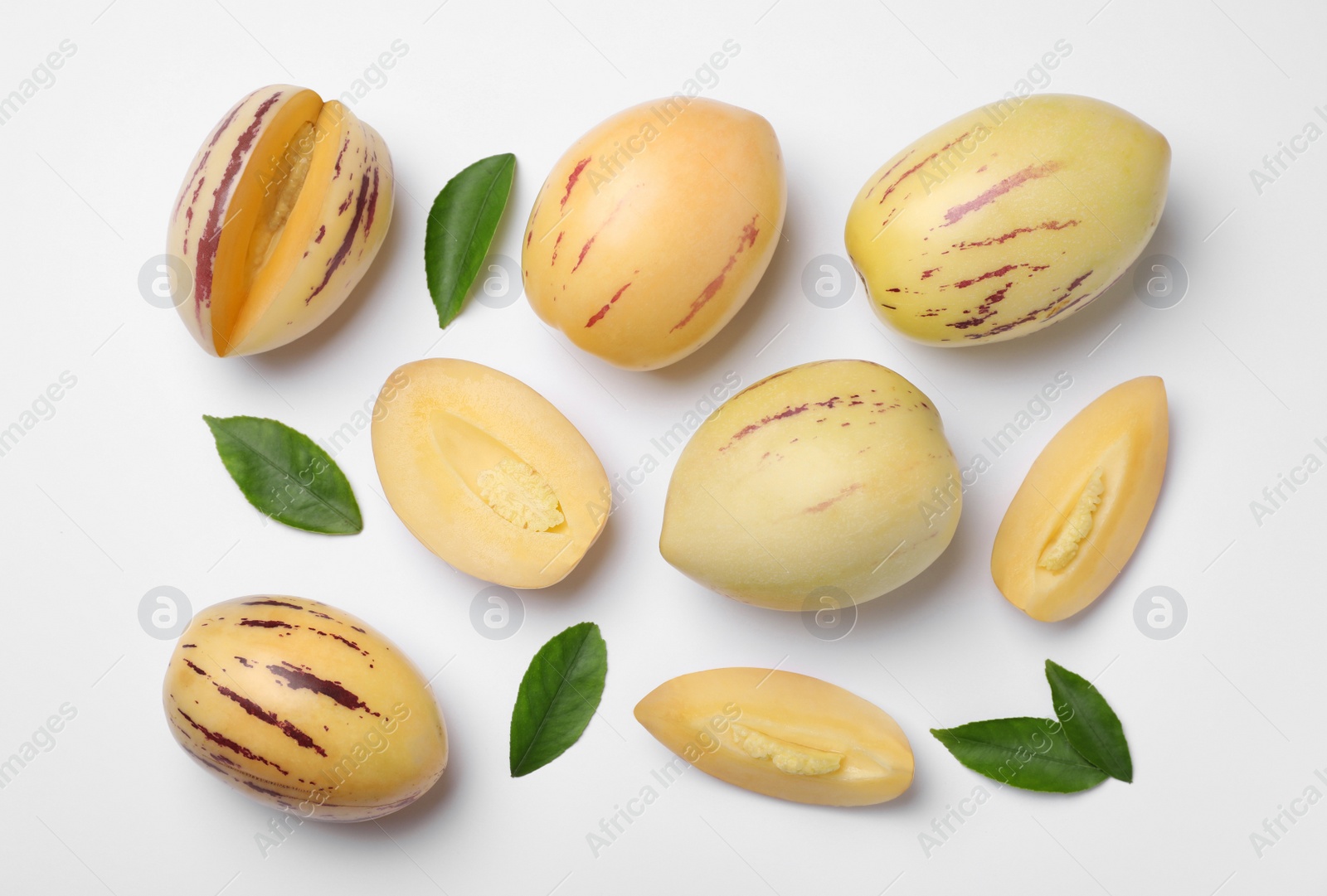 Photo of Whole and cut pepino melons with green leaves on white background, flat lay