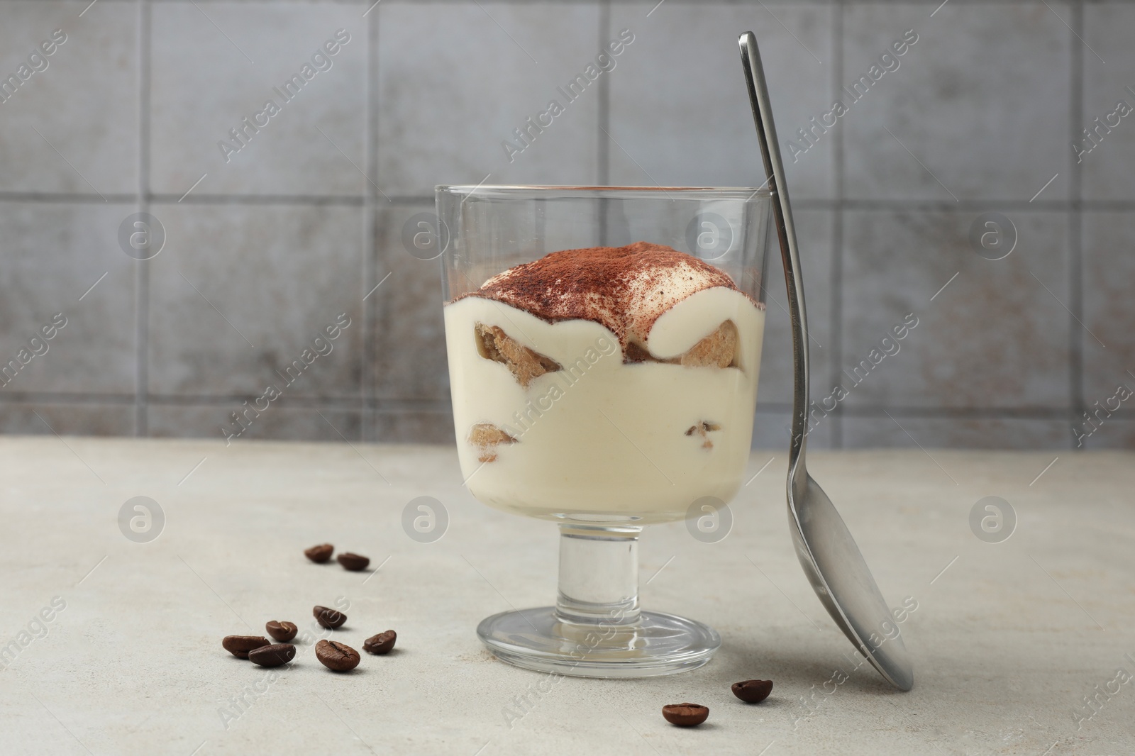 Photo of Delicious tiramisu in glass, spoon and scattered coffee beans on light table