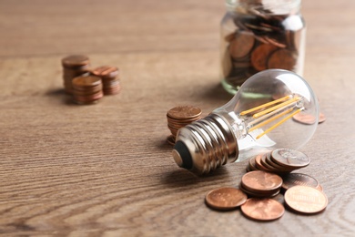 Lamp bulb and coins on wooden table, space for text. Money saving concept