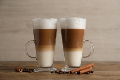 Photo of Hot coffee with milk in glass cups, beans and cinnamon sticks on wooden table