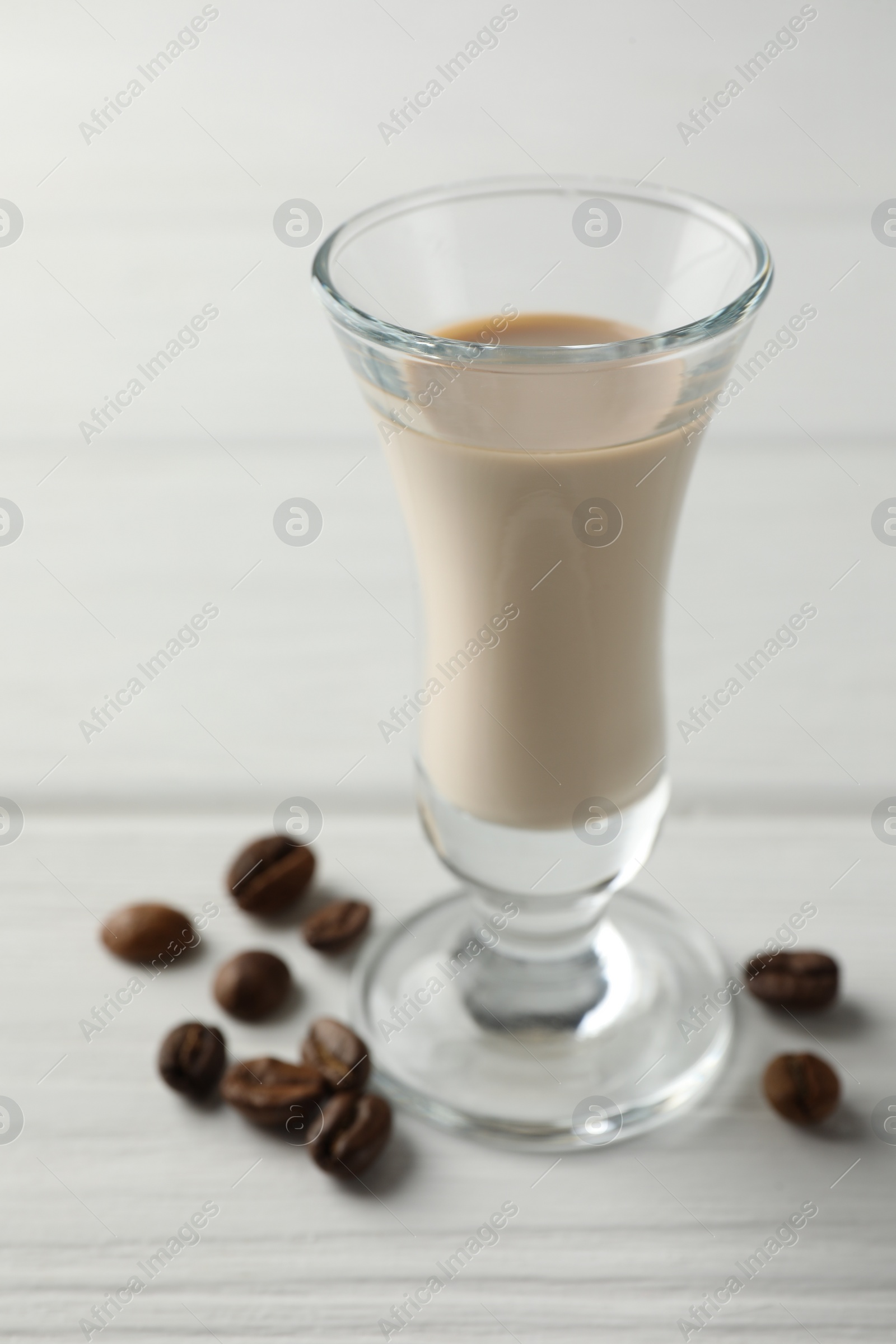 Photo of Coffee cream liqueur in glass and beans on white wooden table