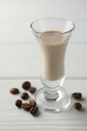 Coffee cream liqueur in glass and beans on white wooden table