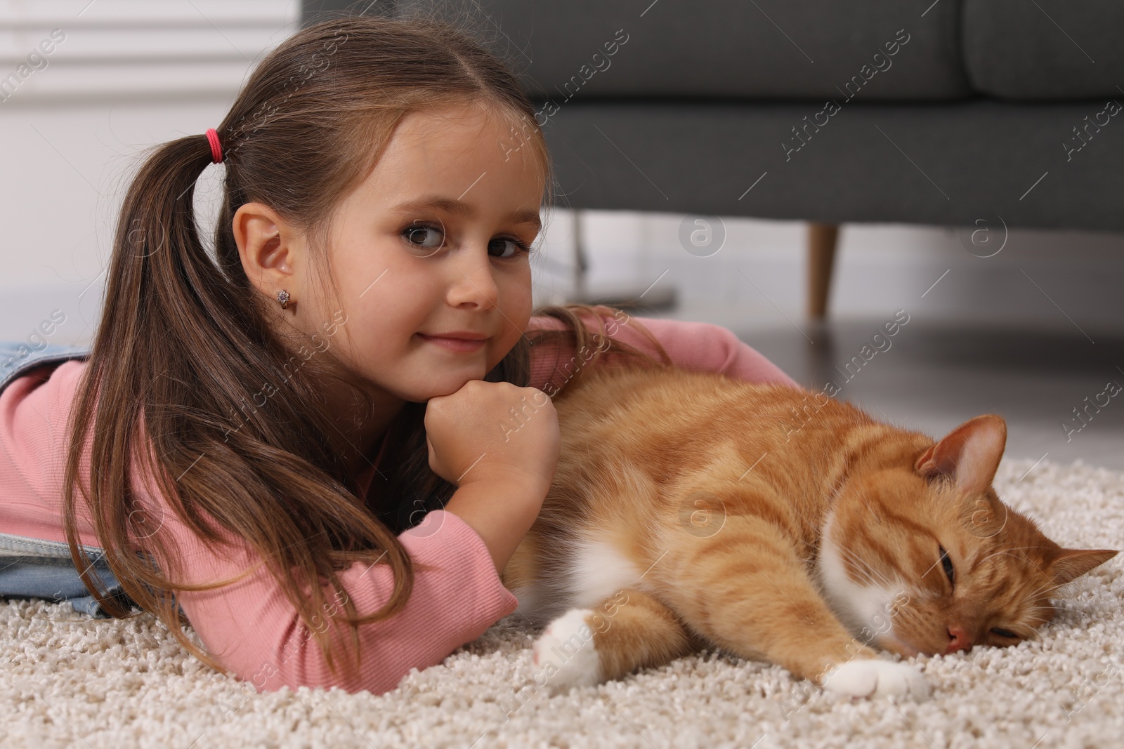 Photo of Little girl and cute ginger cat on carpet at home