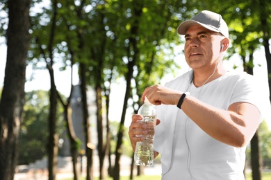 Photo of Handsome mature man with bottle of water in park, space for text. Healthy lifestyle