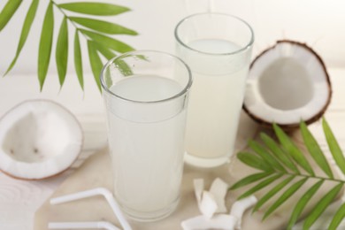 Photo of Glasses of coconut water, palm leaves and nuts on white table