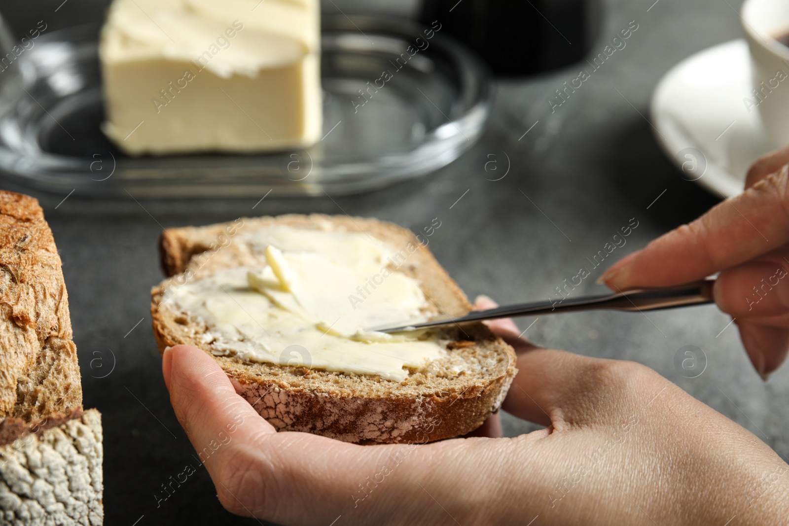 Photo of Woman spreading tasty butter onto bread over grey table, closeup