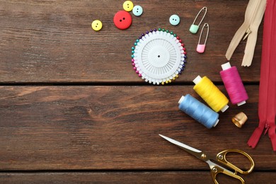 Photo of Threads and other sewing supplies on wooden table, flat lay. Space for text