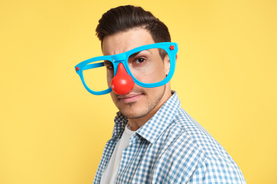 Photo of Man with funny glasses on yellow background. April fool's day