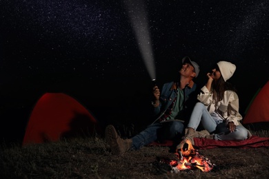 Photo of Happy couple with flashlight near bonfire at night. Camping season