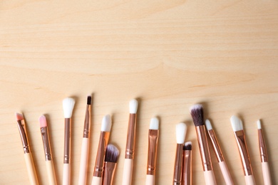 Flat lay composition of professional makeup brushes on wooden background. Space for text