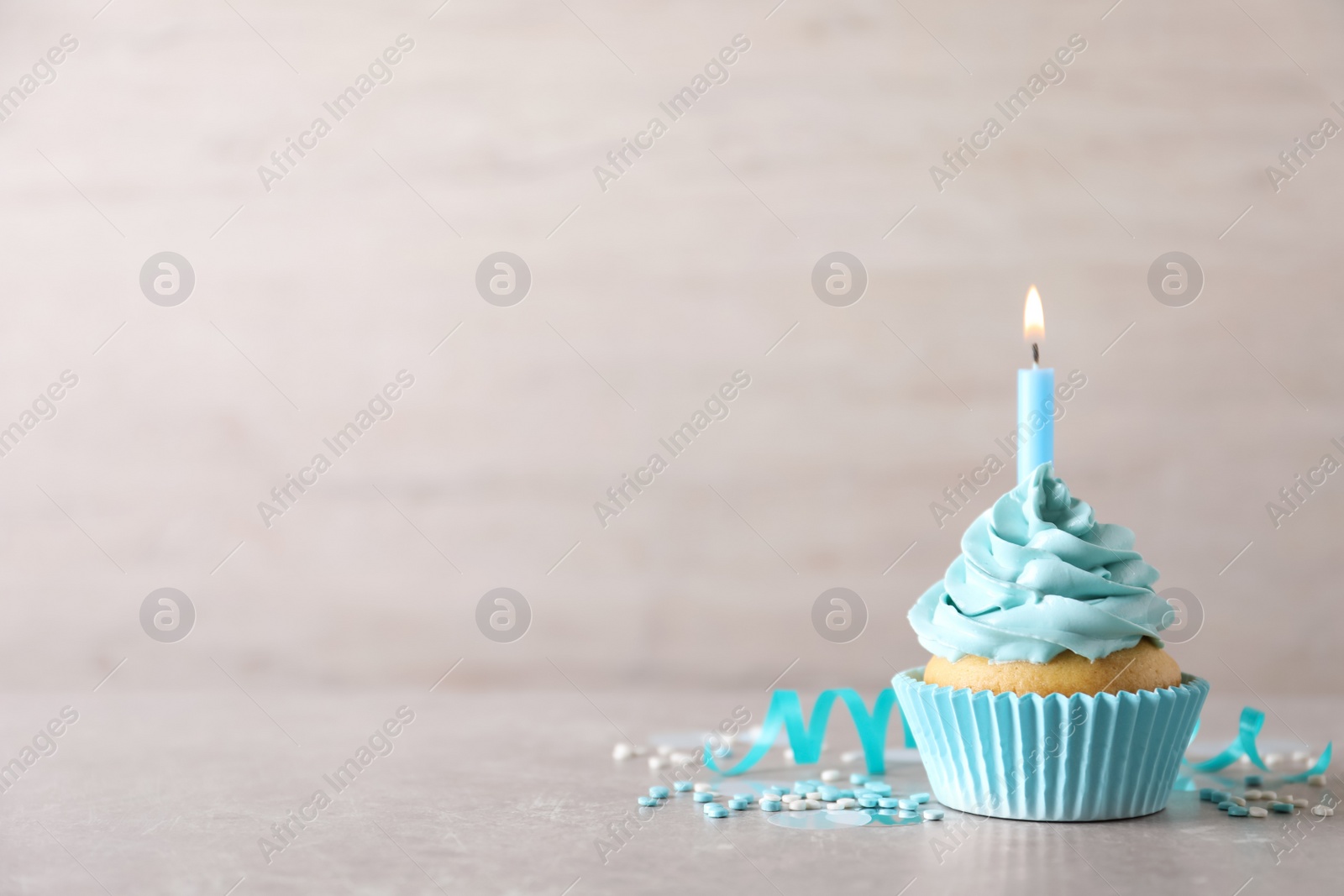 Photo of Delicious birthday cupcake with burning candle, sprinkles and streamer on grey table, space for text