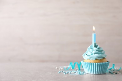 Delicious birthday cupcake with burning candle, sprinkles and streamer on grey table, space for text