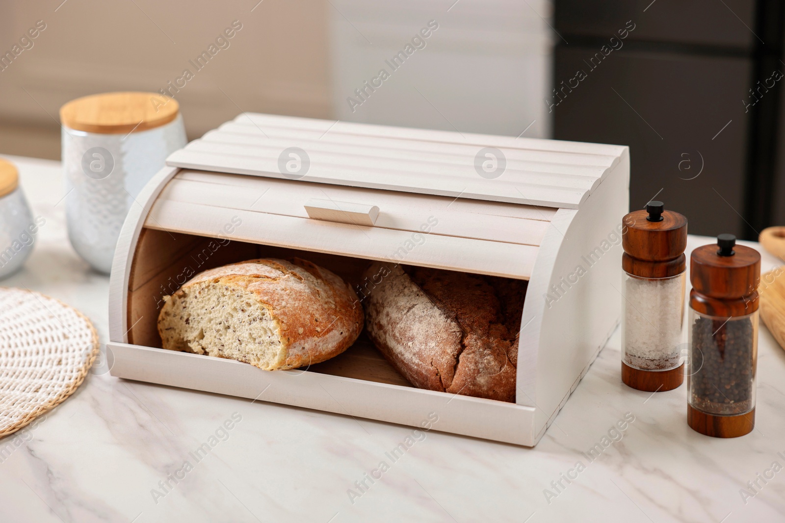 Photo of Wooden bread basket with freshly baked loaves on white marble table in kitchen