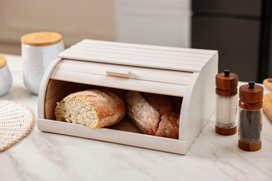 Wooden bread basket with freshly baked loaves on white marble table in kitchen