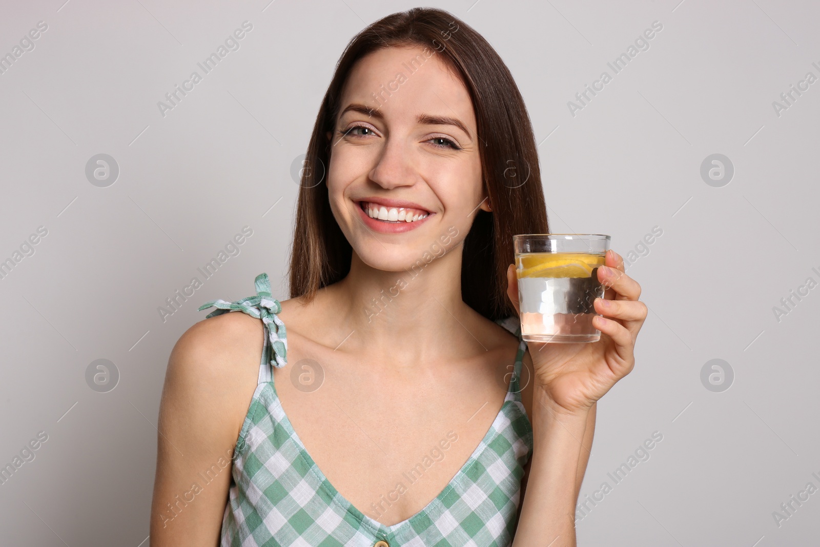 Photo of Young woman with glass of lemon water on light background