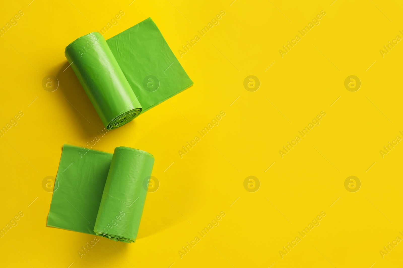 Photo of Rolls of green garbage bags on yellow background, flat lay. Space for text