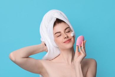 Photo of Young woman washing face with brush and cleansing foam on light blue background