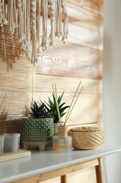 Air reed freshener, houseplant and decor on console table near wooden wall. Interior design