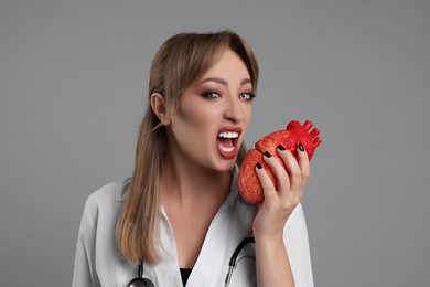 Photo of Woman in scary nurse costume with heart model on light grey background. Halloween celebration