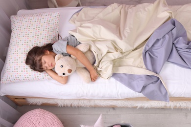 Photo of Little girl sleeping with teddy bear in bed at home