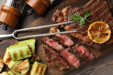 Photo of Delicious grilled beef steak and vegetables served on wooden table, top view