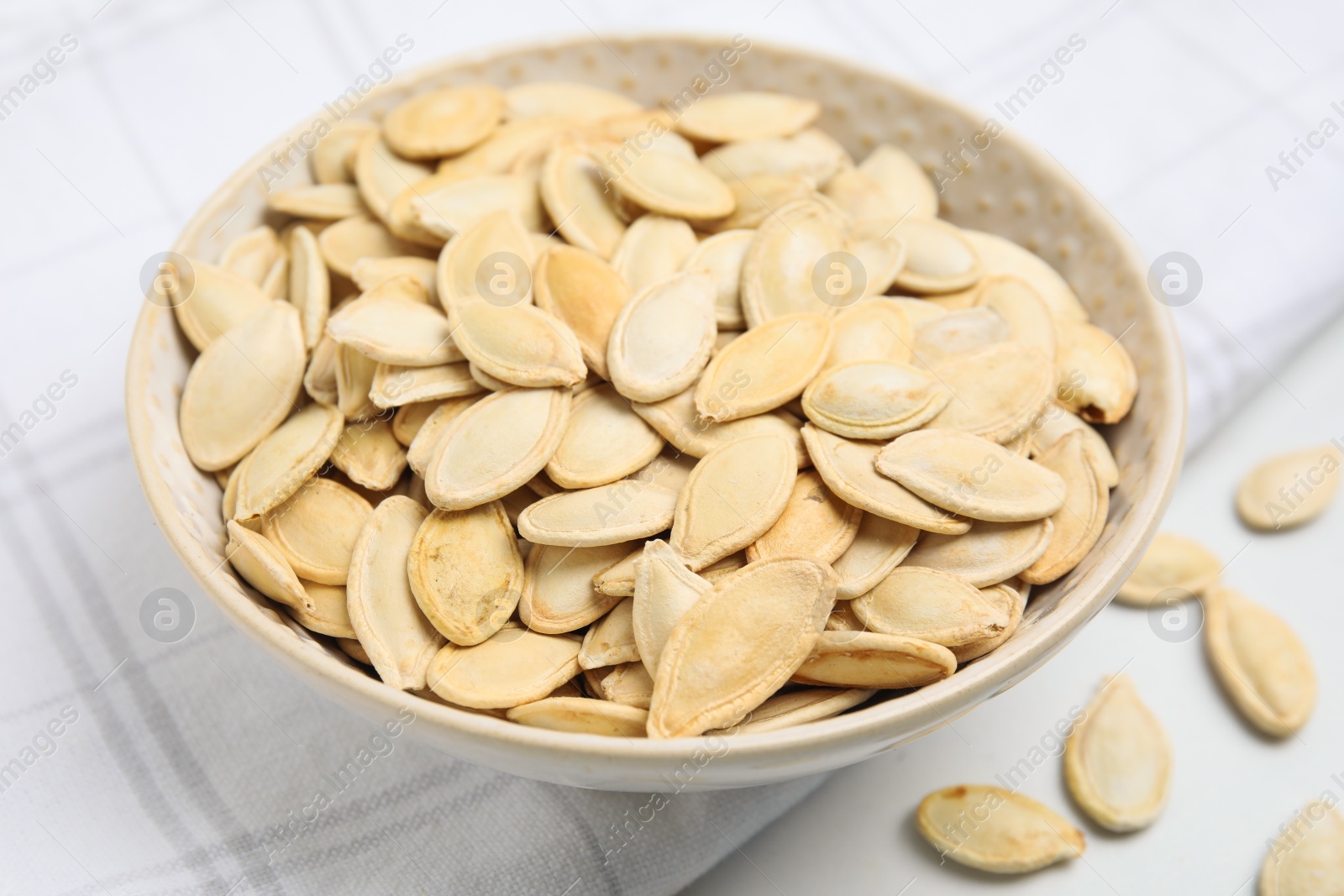 Photo of Bowl with pumpkin seeds on light table, closeup